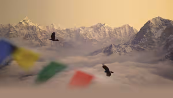 Two birds fly above Himalayan peaks and clouds, with prayer flags fluttering in the foreground