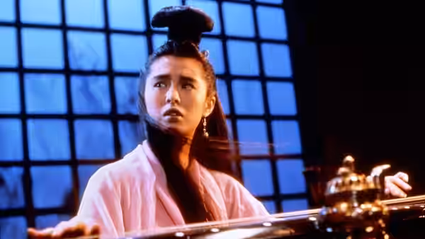 Lip Siu Sin (Joey Wong) sits at a table playing a guqin