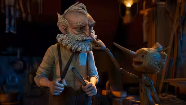 Geppetto (David Bradley) holding tools while facing Pinocchio in the workshop