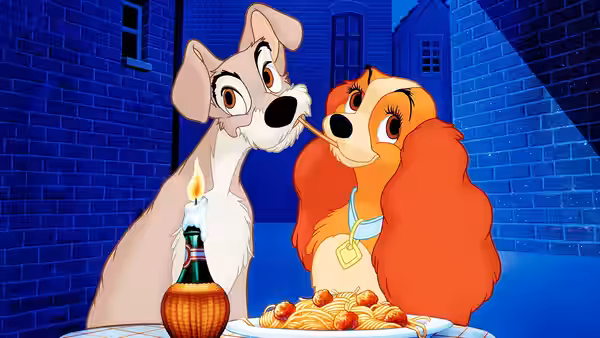 Tramp and Lady share a spaghetti strand nose to nose over a checkered table
