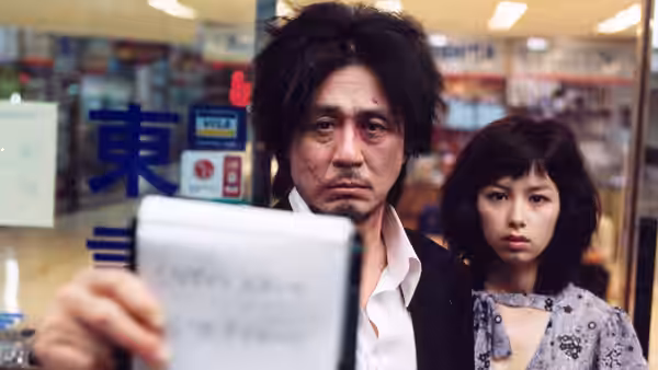 Oh Dae-su (Choi Min-sik) holding a notepad with Mi-do (Kang Hye-jung) standing beside him