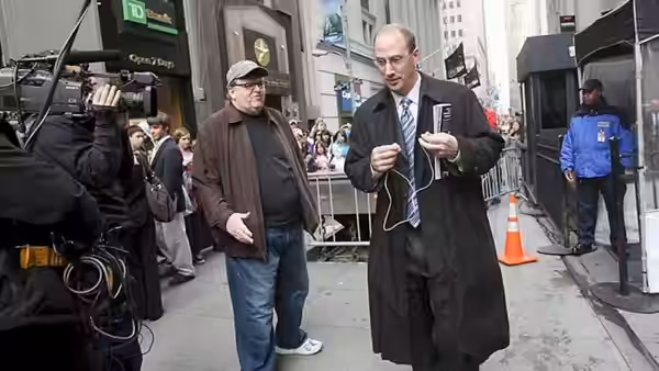 Michael Moore walks beside a suited man past a news camera crew