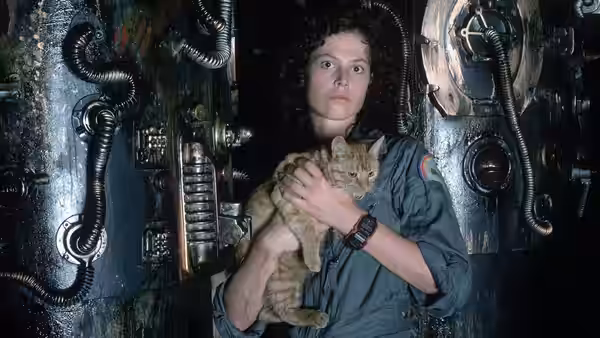 Ripley (Sigourney Weaver) holding a cat in a dimly lit mechanical corridor