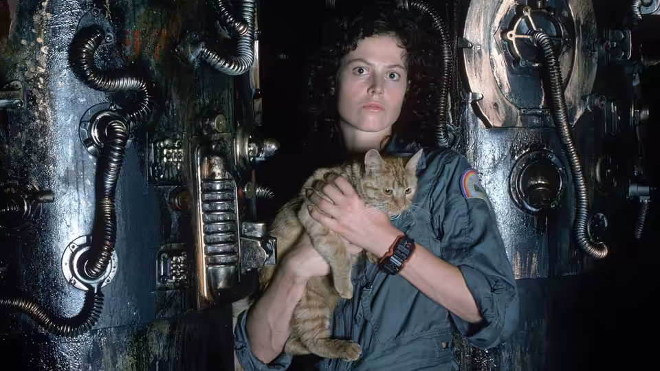 Ripley (Sigourney Weaver) holding a cat in a dimly lit mechanical corridor