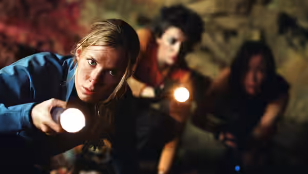 Blonde woman shines flashlight forward in a dark cave