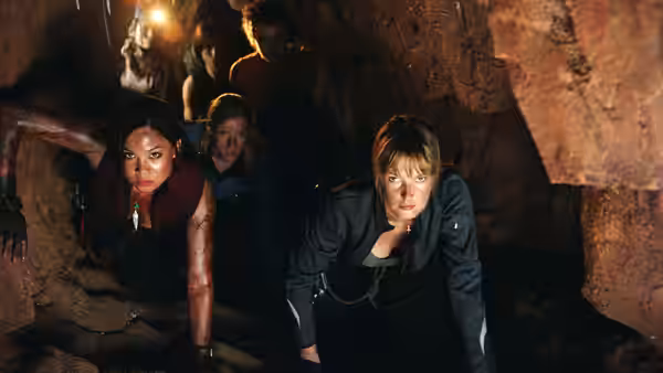 Two women climb through a low rocky cave tunnel