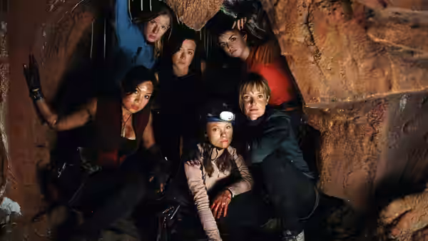 Six women huddle together in a narrow rocky cave passage