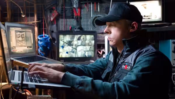 Benji (Simon Pegg) operating laptops while viewing surveillance monitors