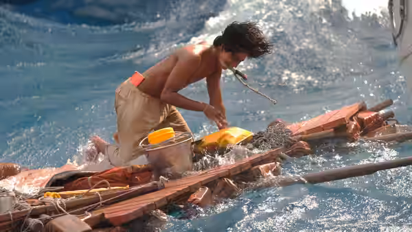 Shirtless young man kneels on wooden raft working in rough ocean waves