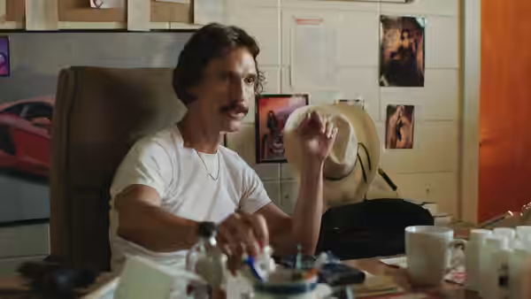 Ron Woodroof (Matthew McConaughey) holds hat while seated at cluttered desk