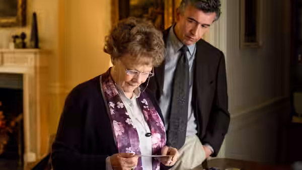 Philomena (Judi Dench) checks her phone indoors as Martin Sixsmith (Steve Coogan) watches