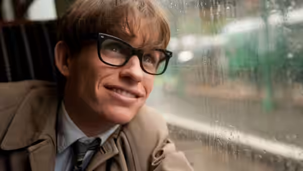 Stephen Hawking (Eddie Redmayne) smiling from his seat beside a rain-streaked window