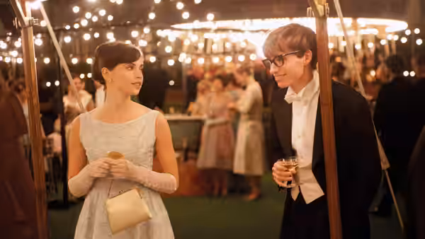 Jane Hawking (Felicity Jones) and Stephen Hawking (Eddie Redmayne) facing each other at a formal gathering