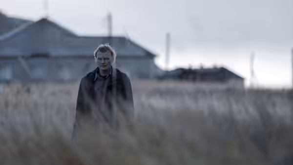 a man standing in tall grass near old buildings