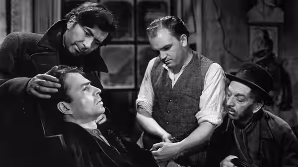 Johnny McQueen (James Mason) lies injured as three men gather around him
