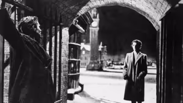 A man raises his arm beneath a stone arch as another waits outside