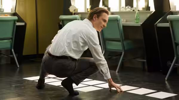 Steve Jobs (Michael Fassbender) crouches touching squares on the floor of a cafe