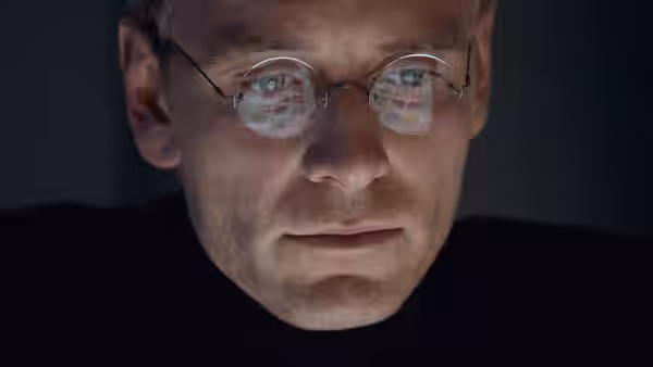 Steve Jobs (Michael Fassbender) looks down with code reflected in round glasses