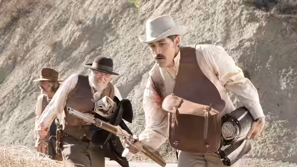 Two armed men with bloodstains standing by a steep rocky slope