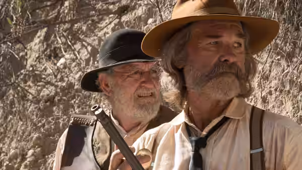 Two older bearded men standing close one holding a rifle