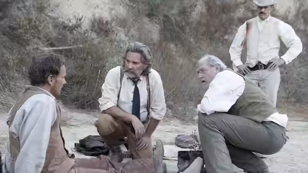 Four men gathered on the ground talking in a rugged clearing