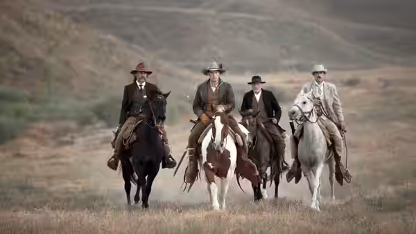 Four men on horseback riding across open grassland in a line