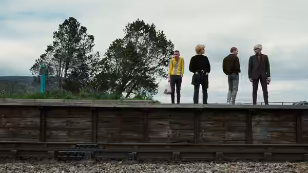 Four people standing on a railway platform overlooking tracks