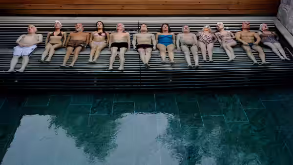 Group of elderly people in swimwear seated in a row above a pool