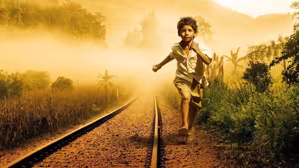 A young boy running barefoot along railway tracks in misty countryside