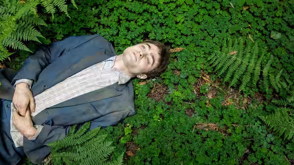 Hank (Paul Dano) lying on his back among green ferns with eyes closed