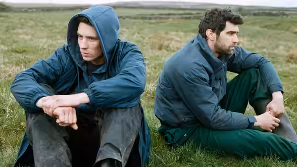 Johnny (Josh O'Connor) and Gheorghe (Alec Secăreanu) sitting on grass in jackets