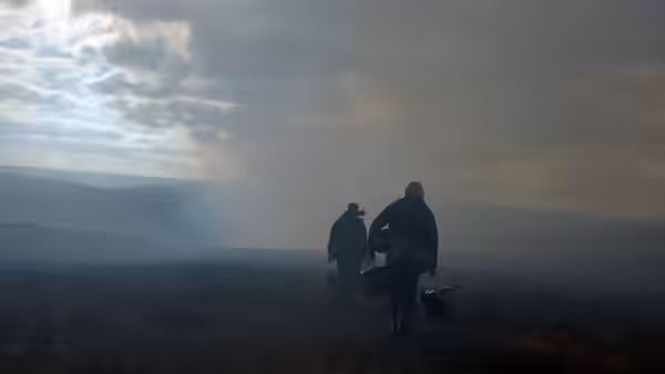 Two men walking away across a misty moor carrying bags