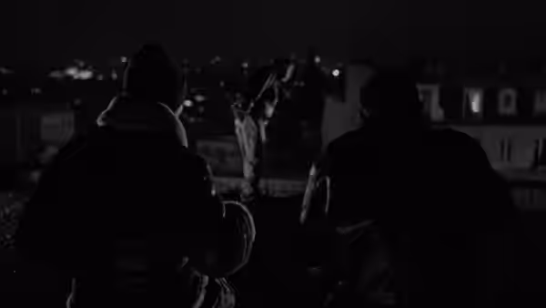 Three men on a rooftop overlooking the city at night