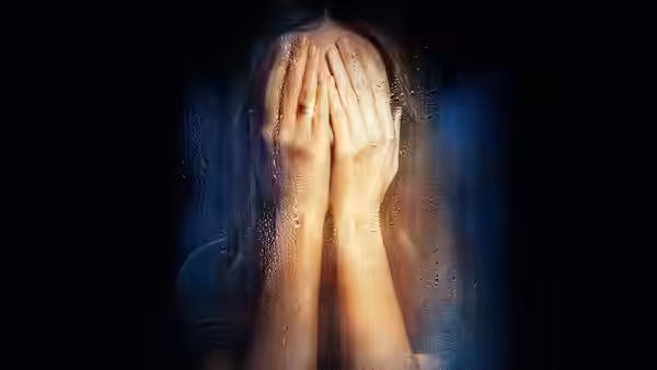 Woman covers face with wet hands against dark wet background