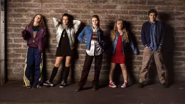 Five young people leaning against a brick wall in casual clothes