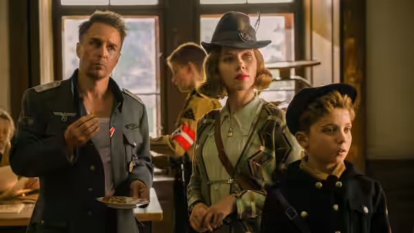 Captain Klenzendorf (Sam Rockwell), Rosie (Scarlett Johansson), and Jojo (Roman Griffin Davis) stand inside a room