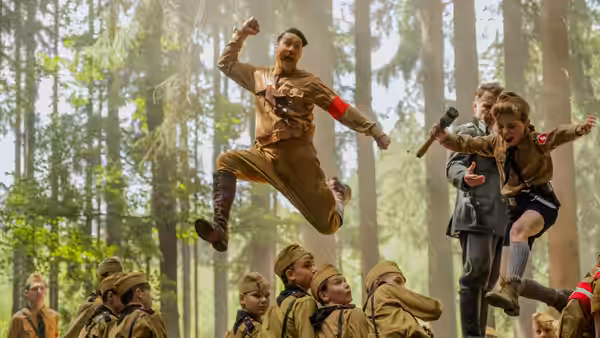 Adolf (Taika Waititi) and Jojo (Roman Griffin Davis) leap among children at a forest youth camp