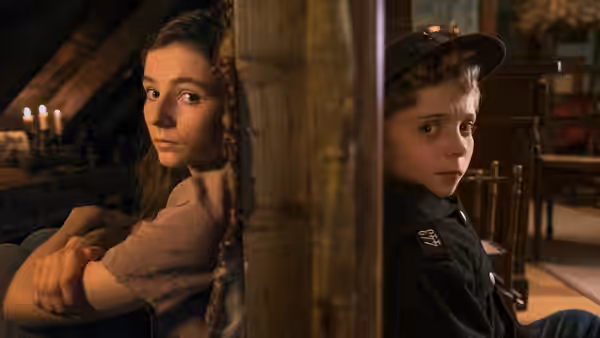Elsa (Thomasin McKenzie) and Jojo hide behind a wooden post indoors