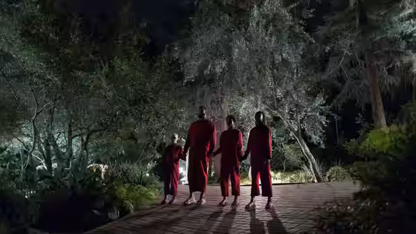 Five people in red jumpsuits holding hands while walking on a path at night