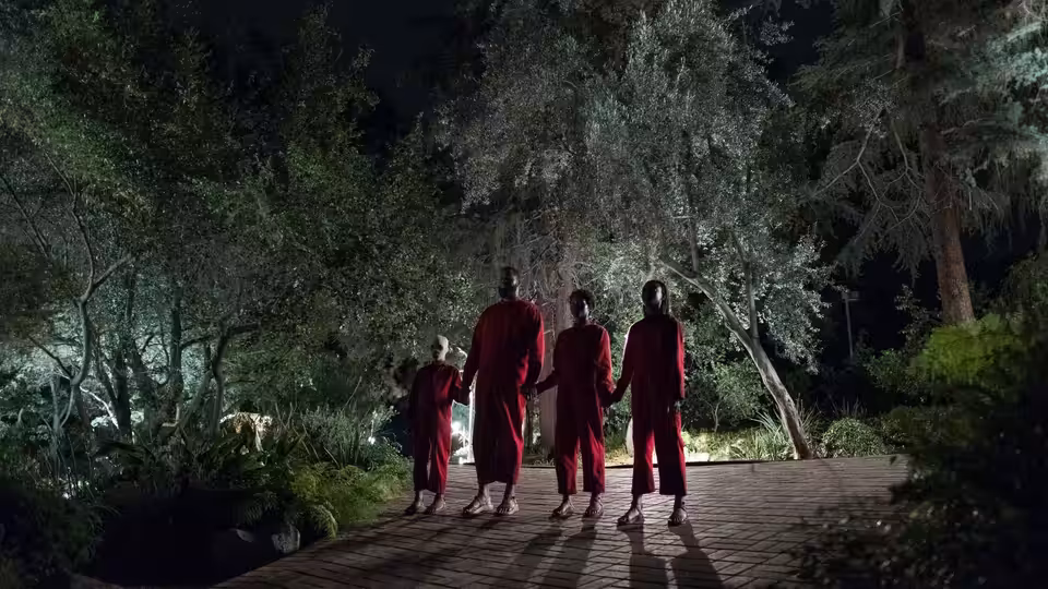 Five people in red jumpsuits holding hands while walking on a path at night