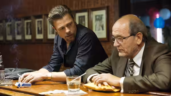 Jackie Cogan (Brad Pitt) leaning across a table toward Mickey (James Gandolfini)