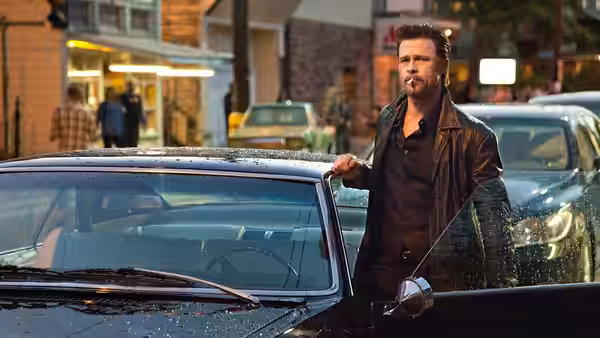 Jackie Cogan (Brad Pitt) standing beside a damaged car on a city street