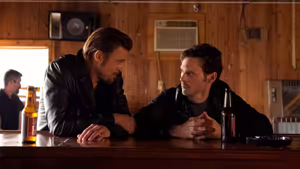 Jackie Cogan (Brad Pitt) and Frankie (Scoot McNairy) talking at a wooden bar counter