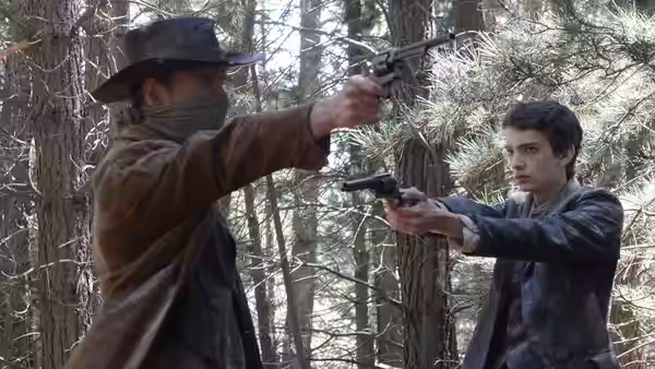Silas (Michael Fassbender) aiming a revolver while Jay (Kodi Smit-McPhee) holds a gun in the woods