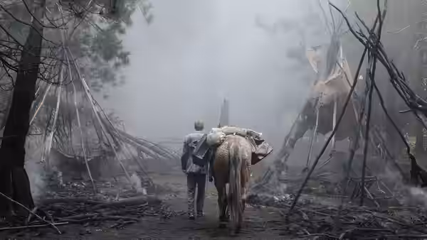 A man carrying a bundle walks through a smoky ruined village