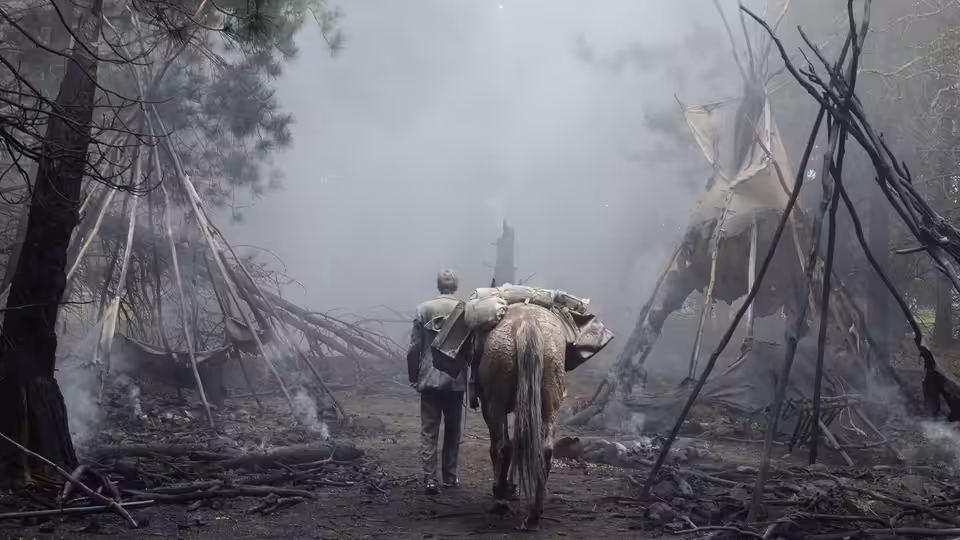 A man carrying a bundle walks through a smoky ruined village