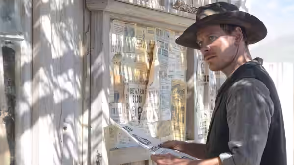 Silas (Michael Fassbender) reading a newspaper outside a wooden building