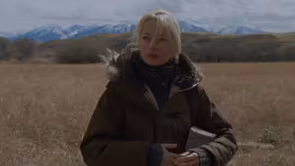 Gina (Michelle Williams) standing in a dry field with mountains behind her