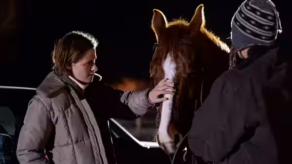 The Rancher (Lily Gladstone) touching a horse's face at night beside another person