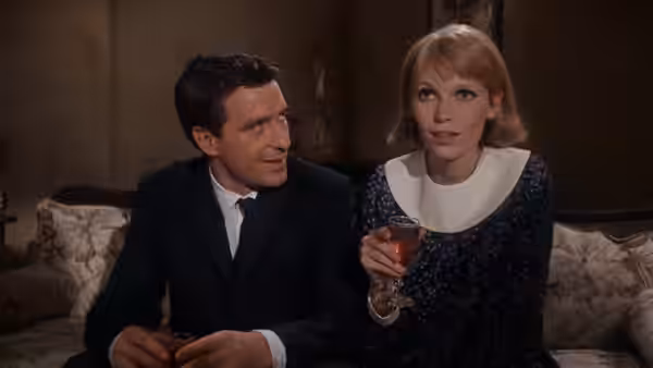 Guy Woodhouse (John Cassavetes) watches Rosemary (Mia Farrow) hold a drink on the sofa